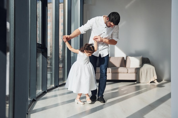 Heureux père avec sa fille en robe apprenant à danser ensemble à la maison