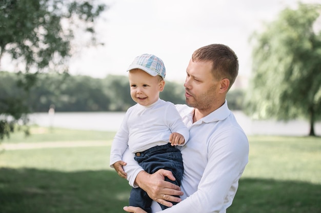 Heureux père avec son petit fils debout dans un parc ensoleillé