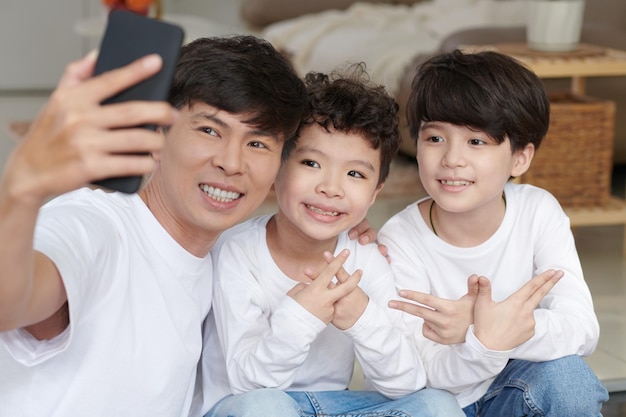 Heureux père souriant et prenant un selfie avec ses deux fils pour publier sur les réseaux sociaux