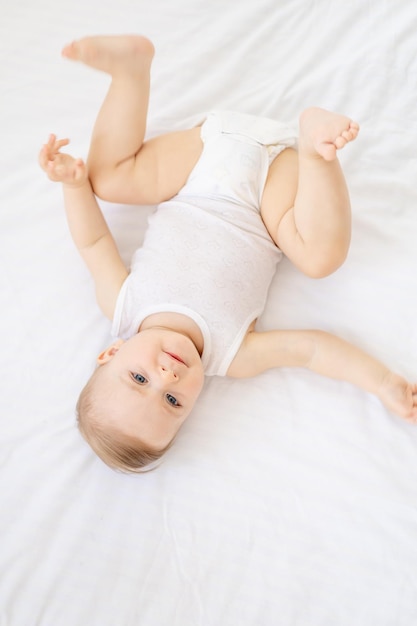 Heureux petit bébé fille ou garçon dans un corsage blanc sur le lit dans la chambre en levant bébé aux yeux bleus