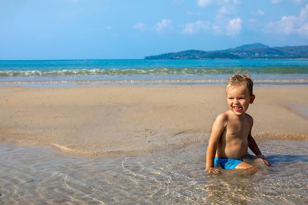 Heureux petit enfant assis dans l'eau au bord de mer en été