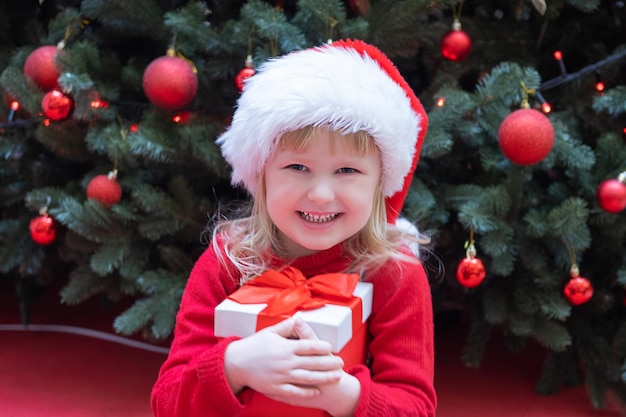 Heureux petit enfant enfant fille en bonnet rouge de santa tenant le cadeau de noël à la main