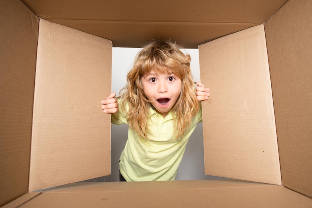 Heureux petit enfant garçon ouvre le cadeau et regarde à l'intérieur de la boîte en carton enfant garçon l'air surpris