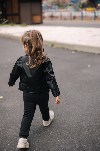 Heureux petit enfant en jaket en cuir écologique noir marchant en plein air en automne