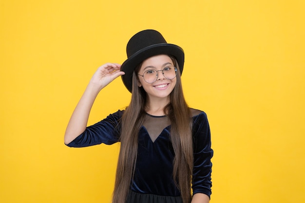 Heureux petit enfant porter une robe de soirée noire avec un chapeau avec un accessoire de fond jaune look fashion