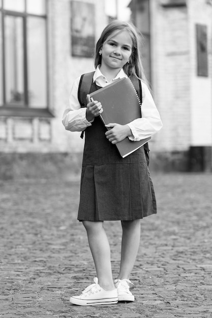 Photo heureux petit enfant en uniforme scolaire tenir des livres de bibliothèque dans la cour d'école en plein air journée de la connaissance