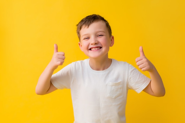 Heureux petit garçon de 7 ans dans un T-shirt blanc sur fond jaune