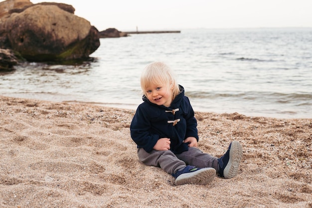 Heureux petit garçon assis sur le sable sur la plage en automne