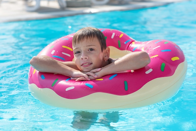 Heureux petit garçon avec bouée de sauvetage panachée sous forme de beignet s'amuse dans la piscine
