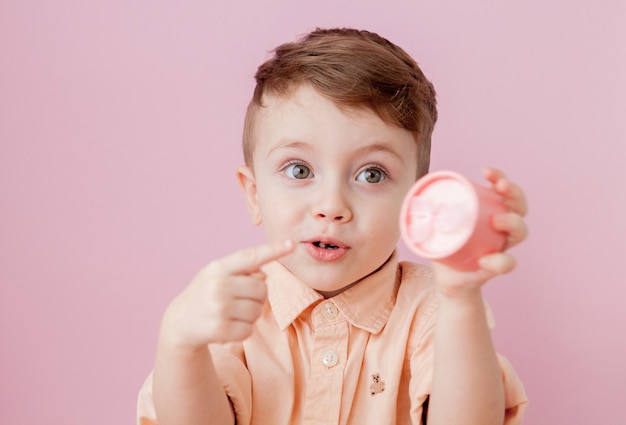 Heureux petit garçon avec un cadeau. Photo isolée sur fond rose. Garçon souriant tient la boîte présente.