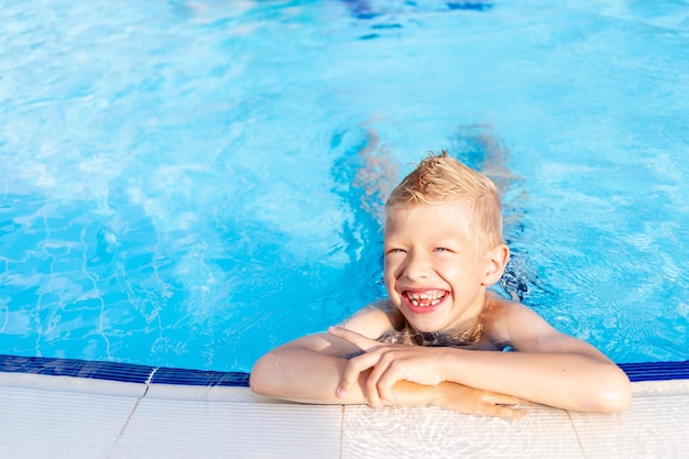 Heureux petit garçon dans la piscine avec de l'eau bleue se baignant et souriant le concept de vacances d'été et de voyage