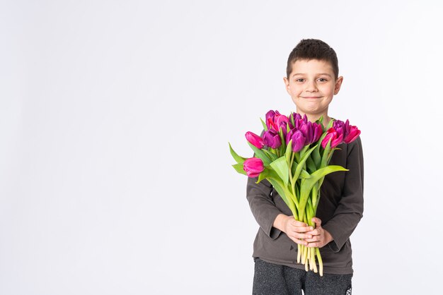 Heureux petit garçon dans des vêtements décontractés avec un bouquet de tulipes isolé sur blanc