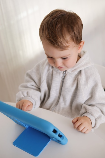 Heureux petit garçon jouant au jeu sur tablette numérique à la maison. Portrait d'un enfant à la maison regardant un dessin animé sur la tablette. Technologie moderne pour les enfants et l'éducation.