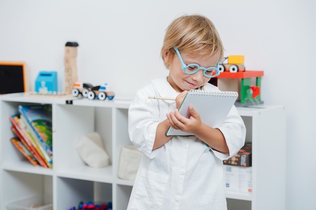 Heureux petit garçon jouant un médecin portant des lunettes jouets et une robe blanche