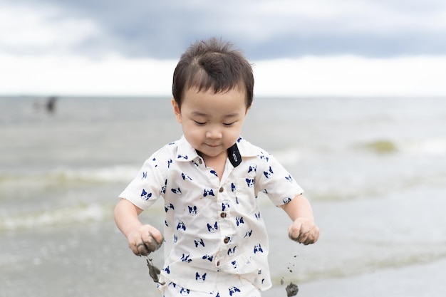 Photo heureux petit garçon jouant sur le sable avec la plage d'été de la mer