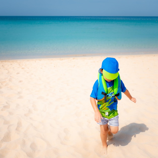 Photo heureux petit garçon jouant sur le sable avec la plage d'été de la mer