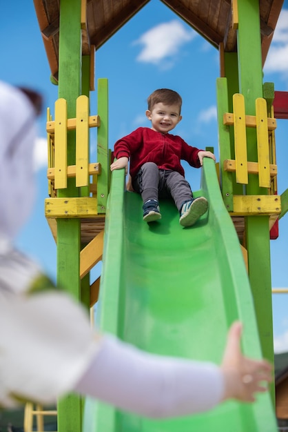 Heureux petit garçon jouant sur un toboggan dans une aire de jeux avec sa mère