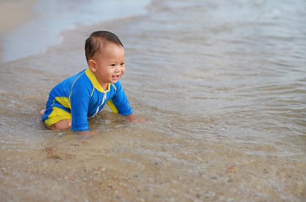 Heureux petit garçon en maillot de bain s&#39;amuser à jouer des vagues de la mer et de l&#39;eau sur la plage.