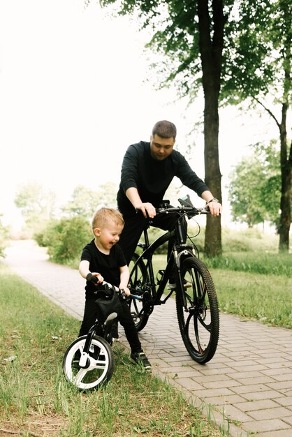 Heureux petit garçon monté sur un vélo avec son père dans le parc