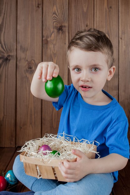 Heureux petit garçon avec un panier d'oeufs de Pâques sur le mur en bois