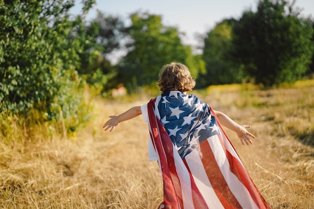 Heureux petit garçon patriote courant sur le terrain avec le drapeau américain. Les États-Unis célèbrent le 4 juillet