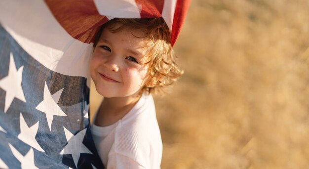 Heureux petit garçon patriote courant sur le terrain avec le drapeau américain. Les États-Unis célèbrent le 4 juillet