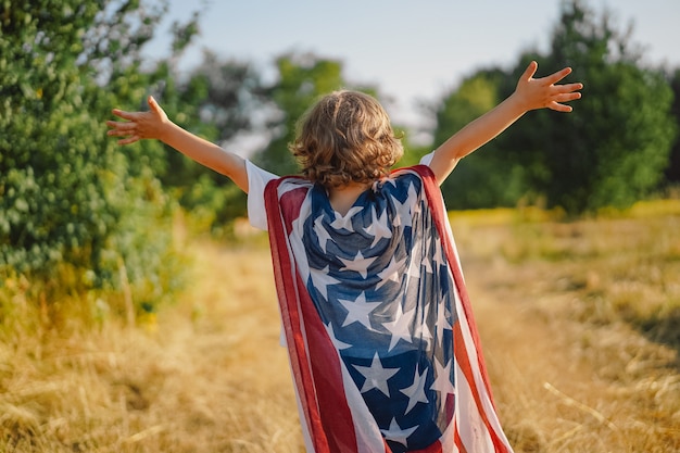 Heureux petit garçon patriote courant sur le terrain avec le drapeau américain. Les États-Unis célèbrent le 4 juillet