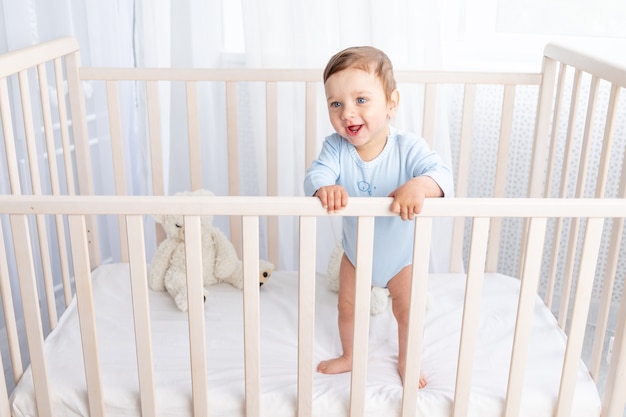 Heureux petit garçon se tient dans le berceau de la pépinière et sourit ou rit