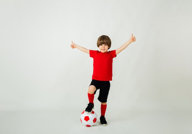 Heureux petit joueur de football garçon se tient avec un ballon de football sur une surface blanche avec un espace pour le texte