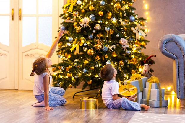 Heureux petits enfants en pyjama regardant l'arbre de Noël dans un beau salon