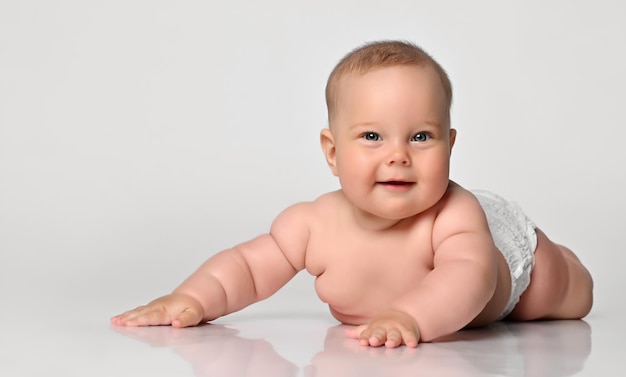 Heureux portrait bébé de six mois fille dans une couche couché sournoisement en vous regardant les bras tendus sur les côtés sur fond blanc