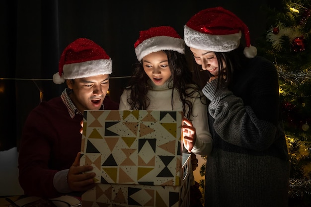 Heureux portrait de famille père mère et fille célèbrent Noël et le nouvel an ensemble ouvrant une boîte-cadeau avec une surprise magique