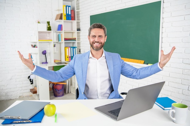 Heureux professeur d'école en classe avec ordinateur au tableau noir