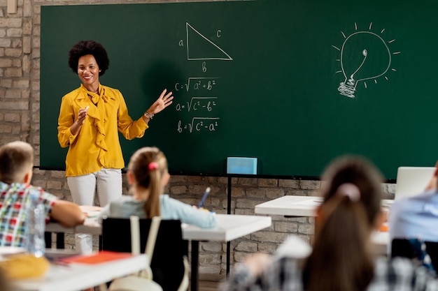 Heureux professeur de mathématiques afro-américain expliquant la conférence sur le tableau noir dans la salle de classe