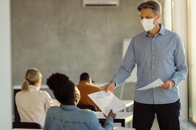 Heureux professeur portant un masque facial tout en donnant les résultats des examens à ses étudiants