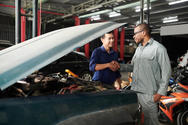 Heureux propriétaire de voiture serrant la main d'un mécanicien après avoir échangé le moteur