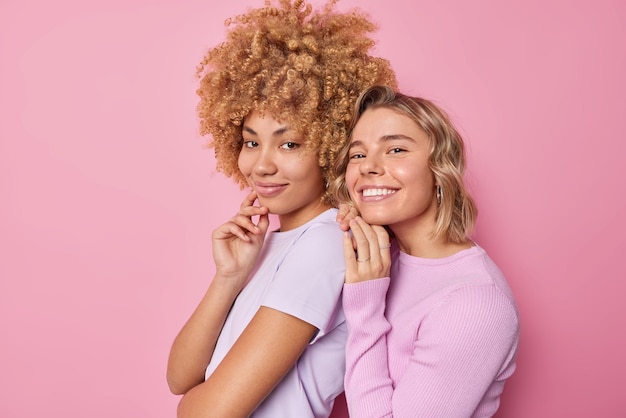 Heureux ravis de jeunes amies se tiennent sur le côté les unes des autres, sourient agréablement de bonne humeur vêtues de vêtements décontractés ont de bonnes relations isolées sur fond rose