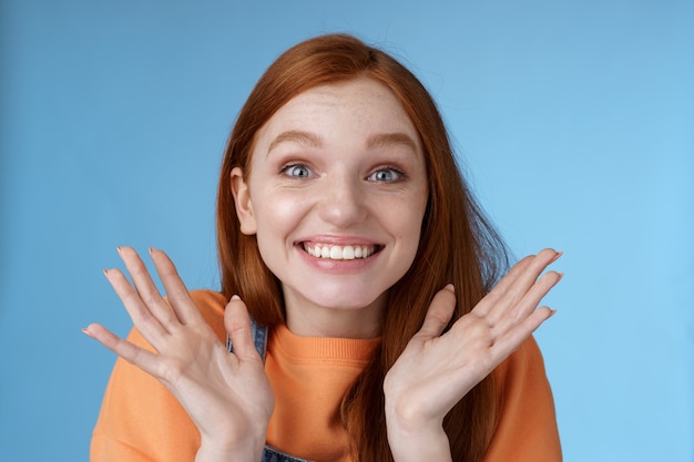 Heureux réjouissant émotionnel jeune fille rousse souriante yeux bleus obtenir des nouvelles excitantes souriant acclamations joyeusement lever les mains ravis yeux grands étonnés surpris accepté célèbre université fond bleu