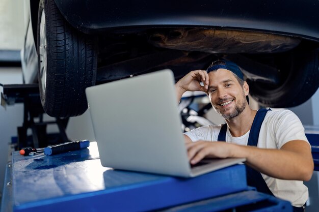 Heureux réparateur à l'aide d'un ordinateur tout en travaillant à l'atelier de voiture