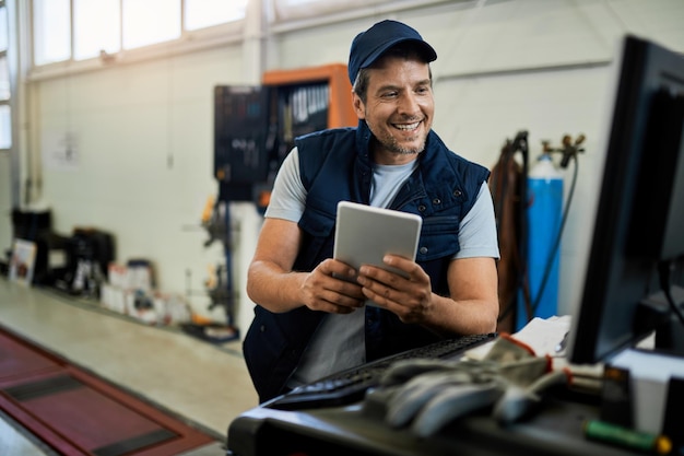 Heureux réparateur automobile utilisant un ordinateur de bureau et une tablette numérique tout en travaillant dans un atelier