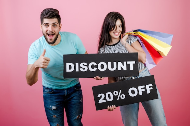 Heureux souriant beau couple homme et femme avec une réduction de 20% sur une enseigne et des sacs colorés