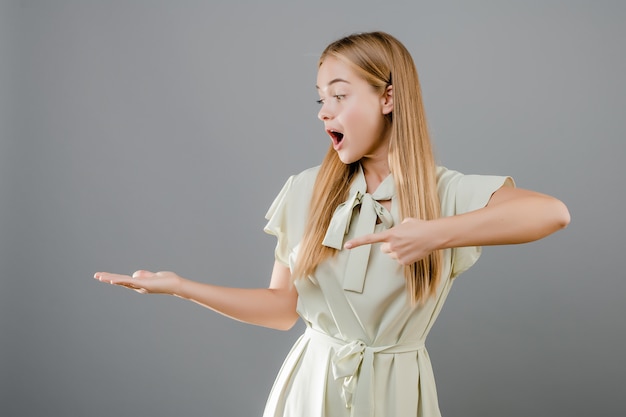 Heureux souriant belle jeune femme blonde pointant le doigt au fond isolé sur gris