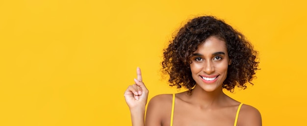 Heureux souriant cheveux bouclés belle femme pointant la main vers le haut pour copier l'espace isolé sur fond de bannière jaune