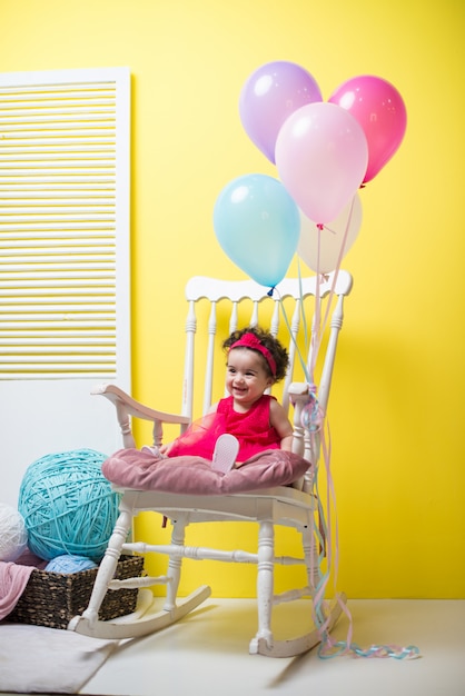 Heureux souriant douce petite fille assise sur le fauteuil avec des ballons d&#39;anniversaire