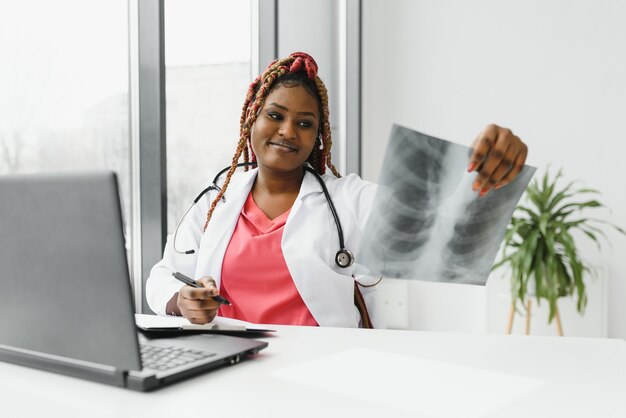 Heureux souriant femme médecin ou infirmière afro-américaine avec casque et ordinateur portable ayant une conférence ou un appel vidéo