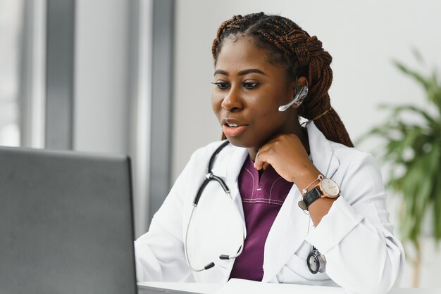 Heureux souriant femme médecin ou infirmière afro-américaine avec casque et ordinateur portable ayant une conférence ou un appel vidéo