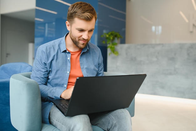 Heureux souriant homme de travail en ligne à distance en tenue décontractée avec ordinateur portable dans un geste gagnant joyeux et réussi assis dans un bureau de coworking à un bureau