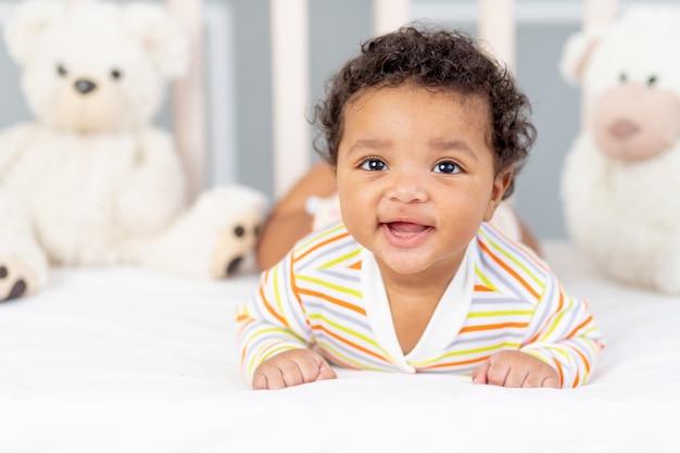 Heureux et souriant petit bébé afro-américain au lit avec des jouets