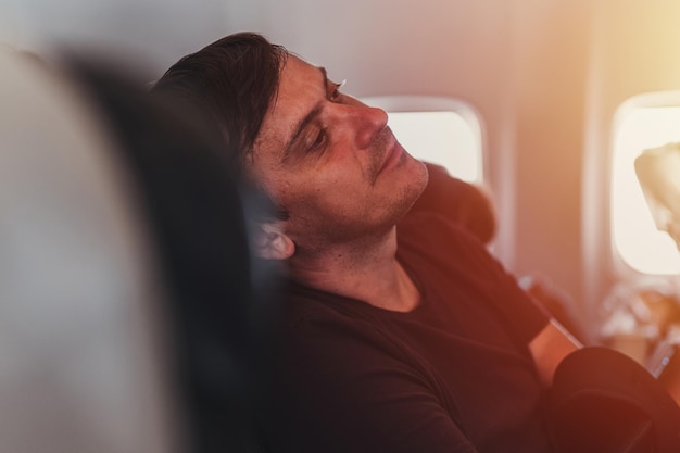 Heureux souriant rêvant de personnes mal rasées un homme de 40 ans avec du chaume est assis sur un avion pendant un vol de l'aéroport pour voyager en passant du temps sur la fusée éclairante de l'avion