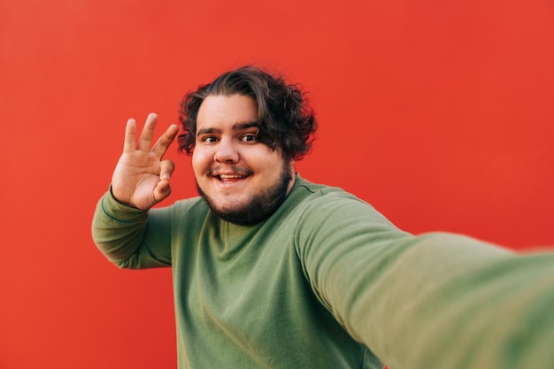 Heureux souriant séduisant jeune homme prend une photo de selfie sur un appareil photo et montre un geste ok